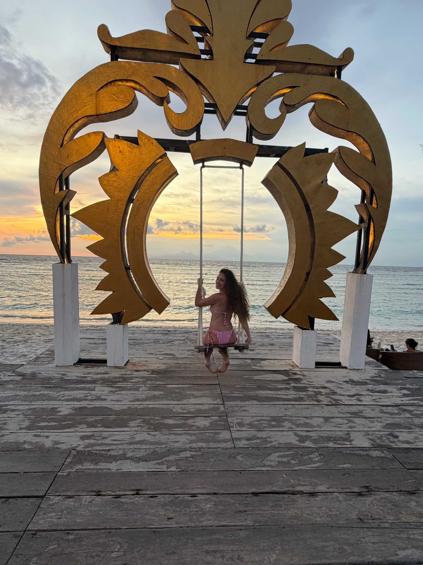 En el columpio bajo la puerta dorada balinesa al atardecer en la playa