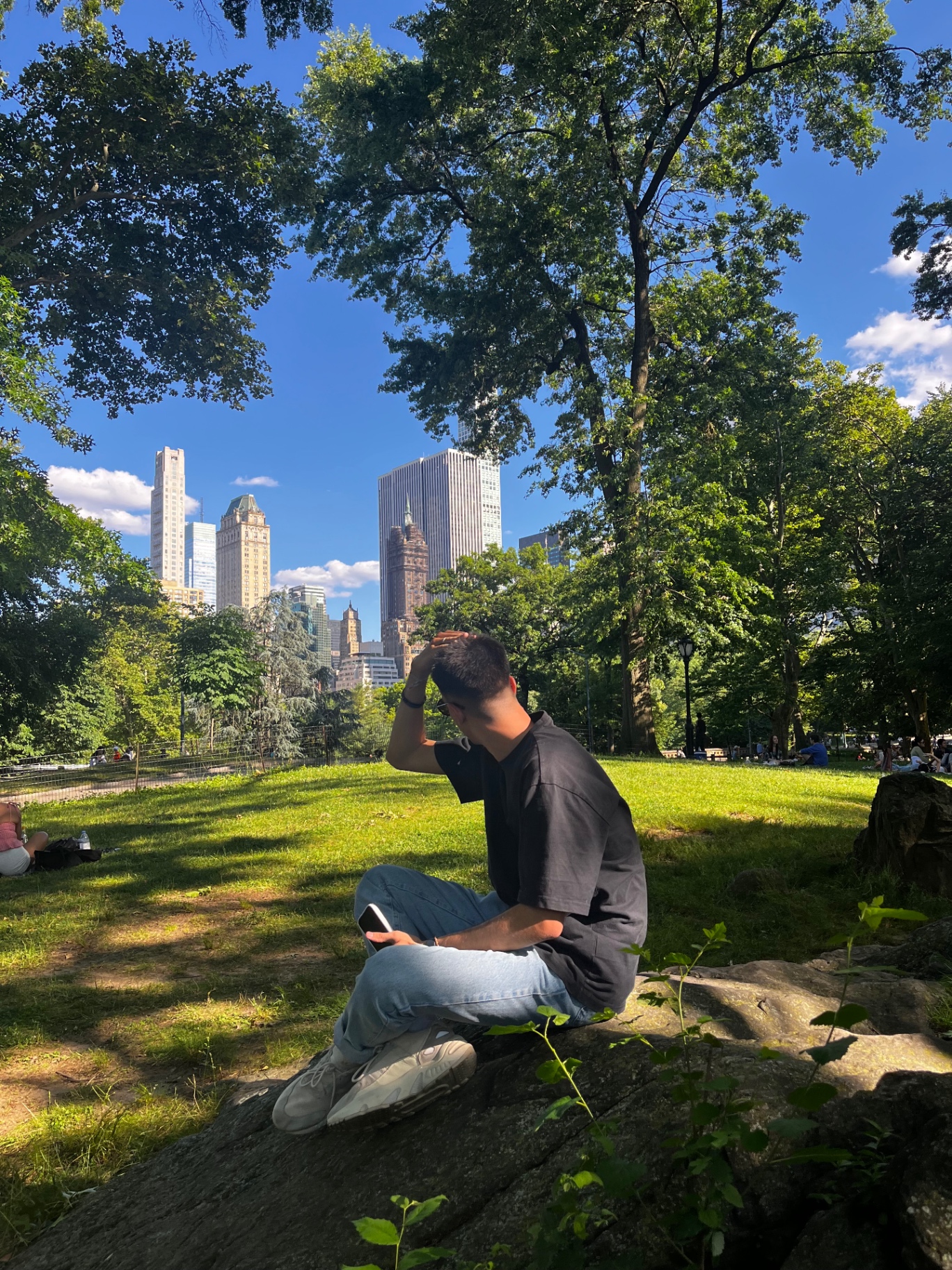 Sentado en una roca de Central Park con el skyline de Midtown al fondo